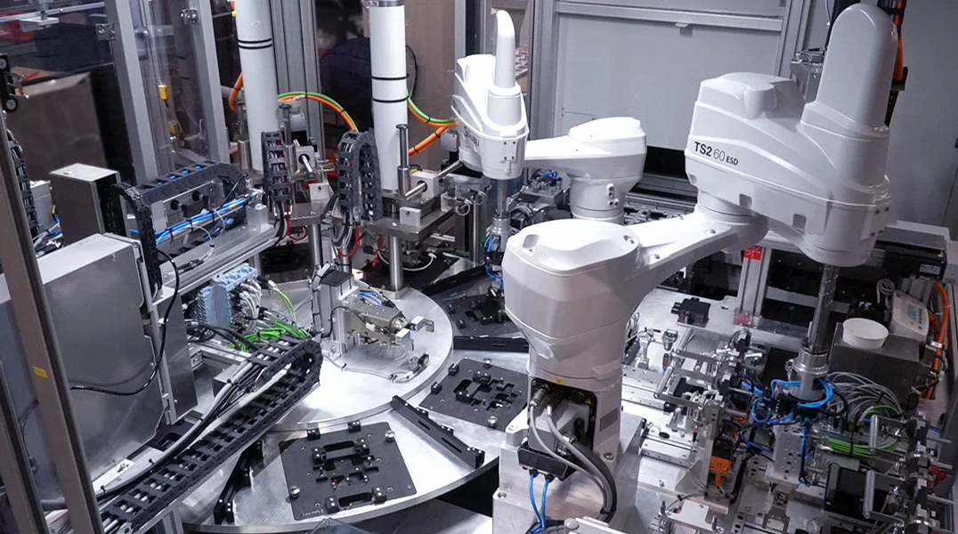 Innenraum einer Montage- und Prüfanlage. Der Bauteiltransport wird mittels eines Rundschalttisches realisiert. Roboter versorgen die Prozesse Dispensen und End-of-Line Prüfung mit Produkten.